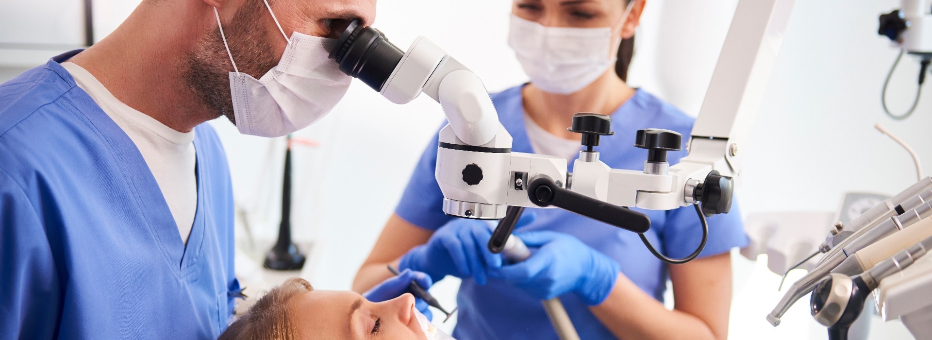 Männlicher Zahnarzt bei der Arbeit mit einem Dentalmikroskop